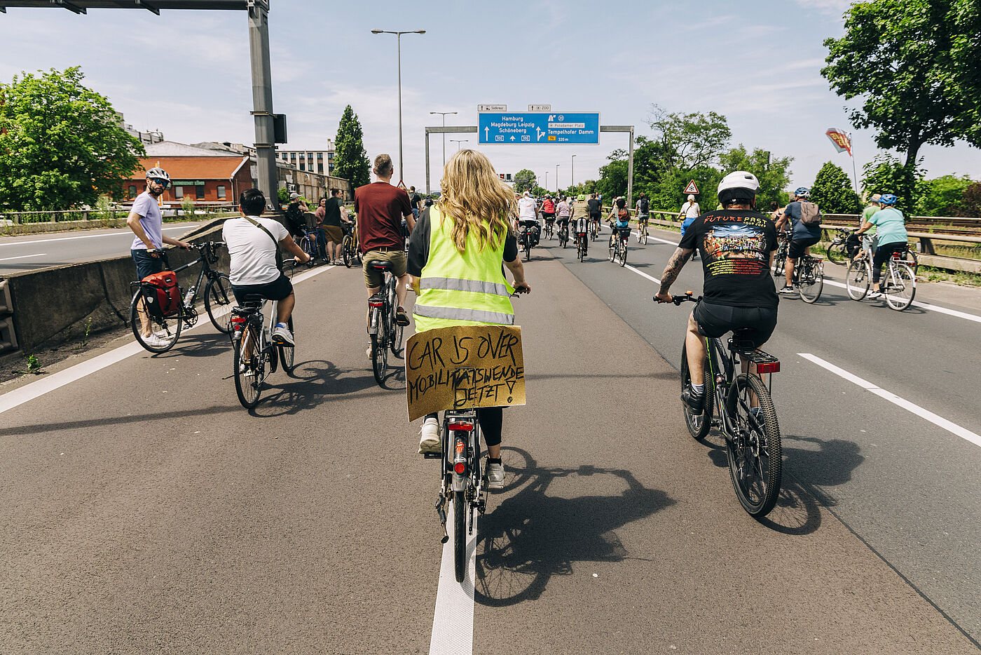 Radfahrende auf der Autobahn bei der Sternfahrt. Frau mit Warnweste und "Car is over" Schild
