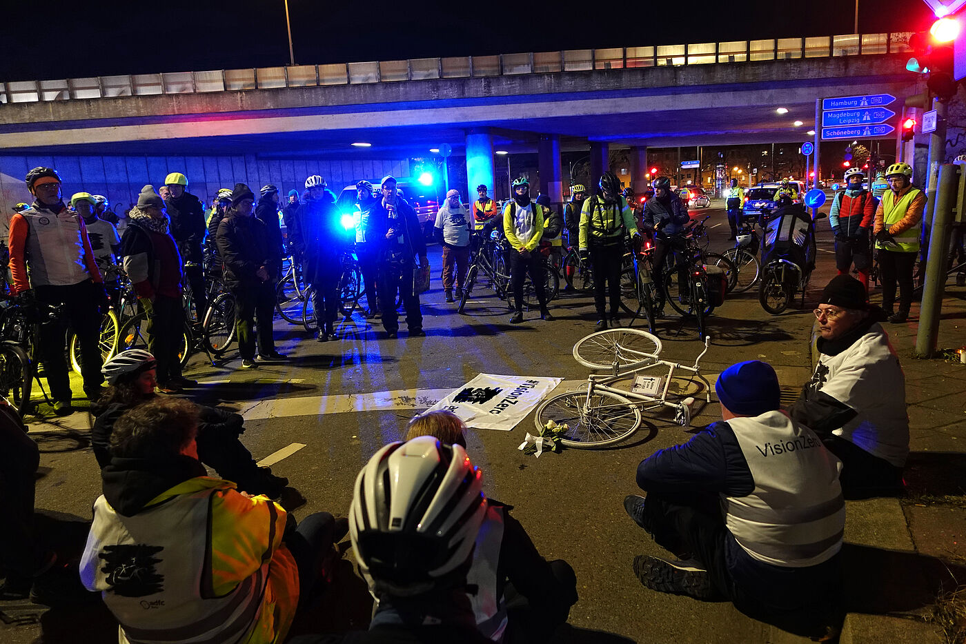 Geisterrad 1.12.2025 Tempelhof Menschen sitzen bei einer Mahnwache um ein weißes Fahrrad auf der Straße
