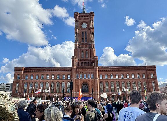 Ein Menschenmenge mit Fahnen und Transparenten vor dem Roten Rathaus Berlin ist zu sehen. 
