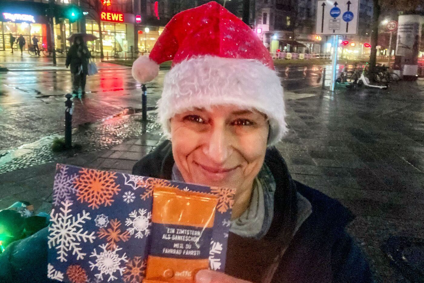 Claudia mit Weihnachtsmütze auf zeigt glücklich eine der Postkarten mit Zimtstern, die verteilt werden.