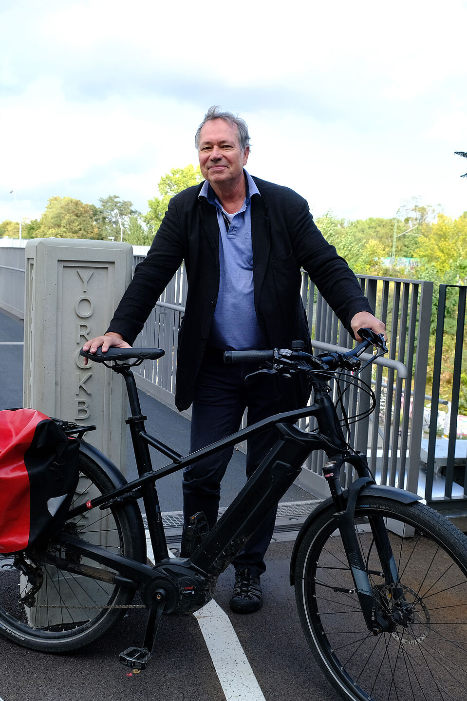 Tilman Bracher Tilman Bracher steht mit seinem schwarzem Fahrrad an einem Radweg.