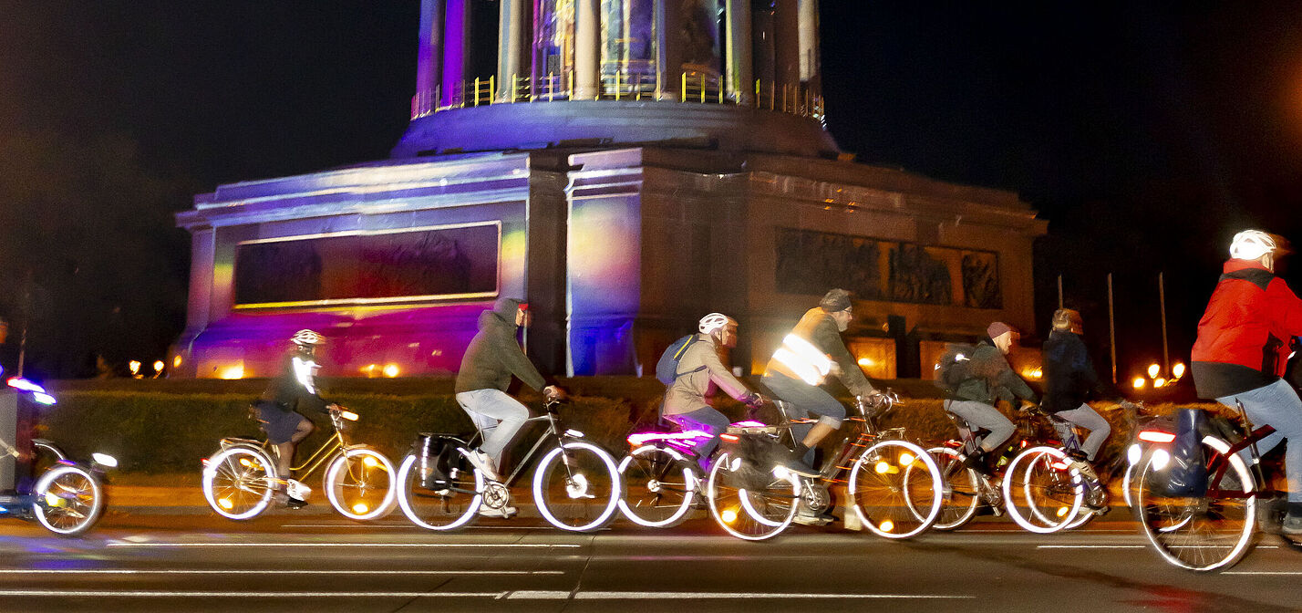 Radfahrende auf erleuchteten Rädern fahren vorbei an der Siegessäule