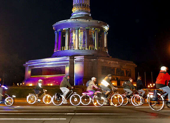 Radfahrende auf erleuchteten Rädern fahren vorbei an der Siegessäule