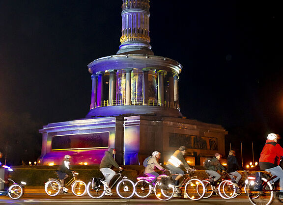 Radfahrende auf erleuchteten Rädern fahren vorbei an der Siegessäule