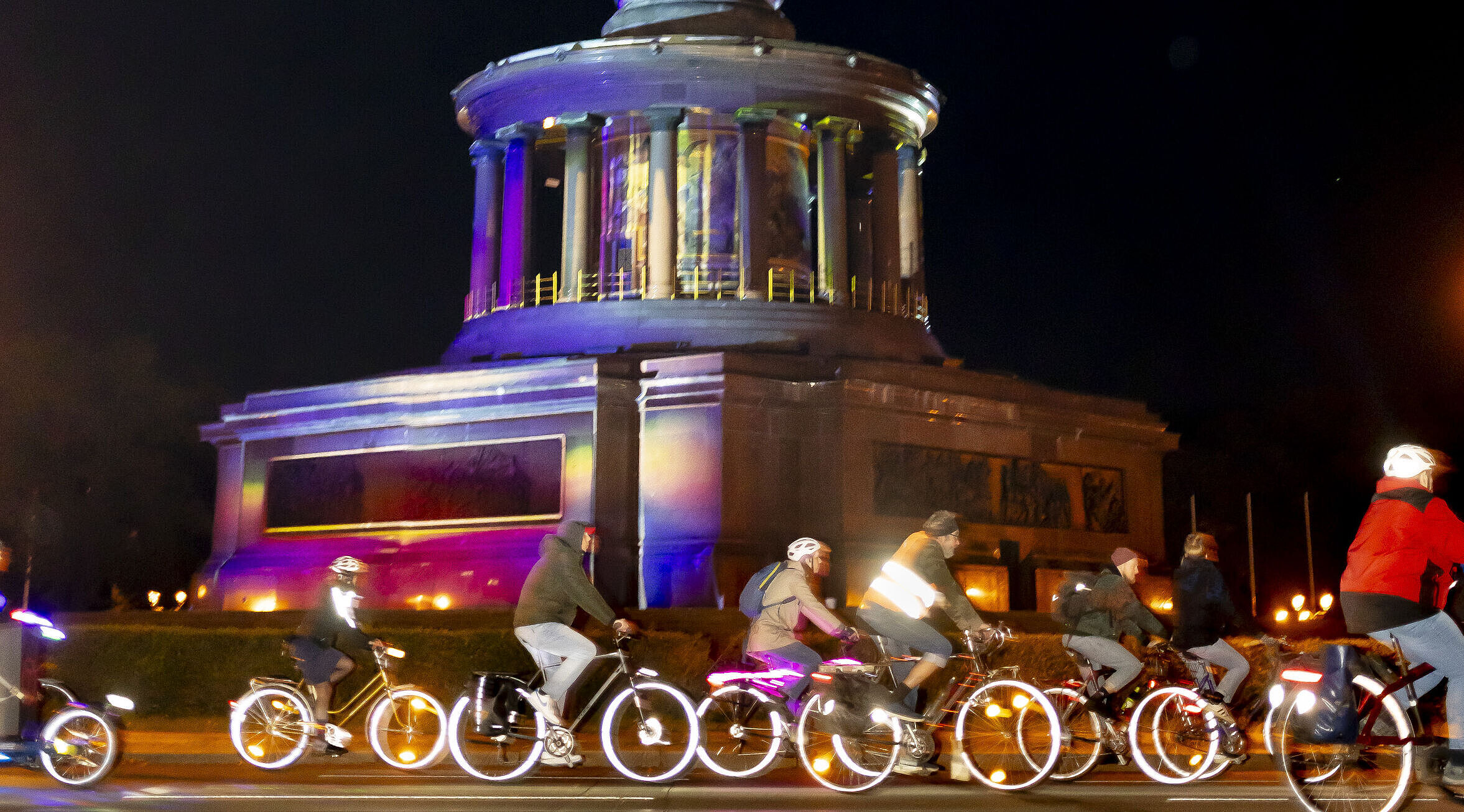 Radfahrende auf erleuchteten Rädern fahren vorbei an der Siegessäule
