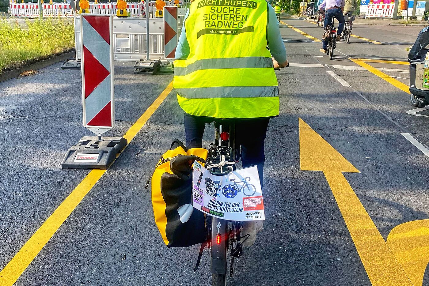 Eine Frau fährt mit dem Fahrrad in einer Demo auf der Filandastraße. Sie trägt eine gelbe Weste mit der Aufschrift "Suche sicheren Radweg" von Changing Cities