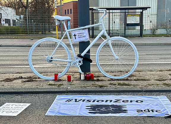 ein weißes Geisterrad mit Informationsschild "Radfahrer 63 Jahre" und Vision Zero Fahne im Vordergrund