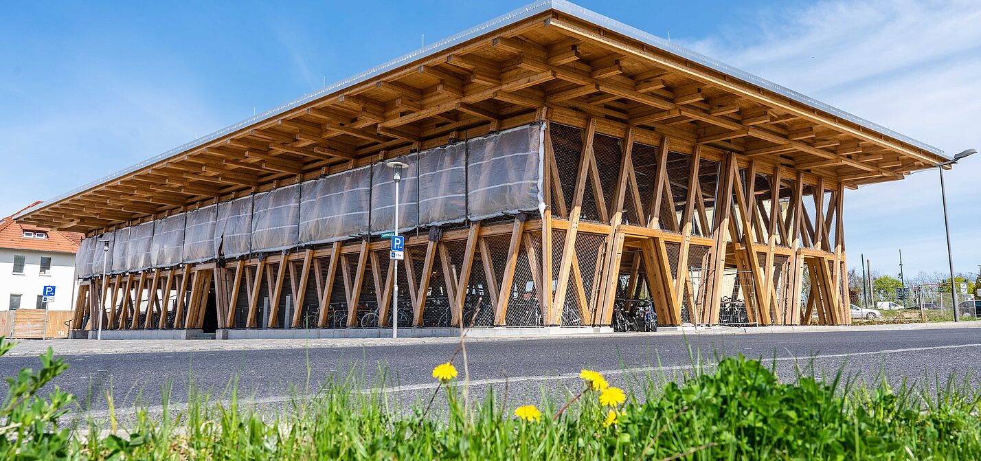 Eine Fahrradparkhaus in Holzkonstruktion vor blauem Himmel und grüner Wiese