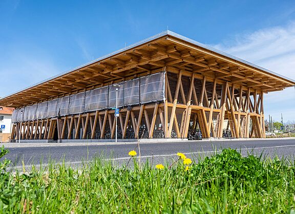 Eine Fahrradparkhaus in Holzkonstruktion vor blauem Himmel und grüner Wiese