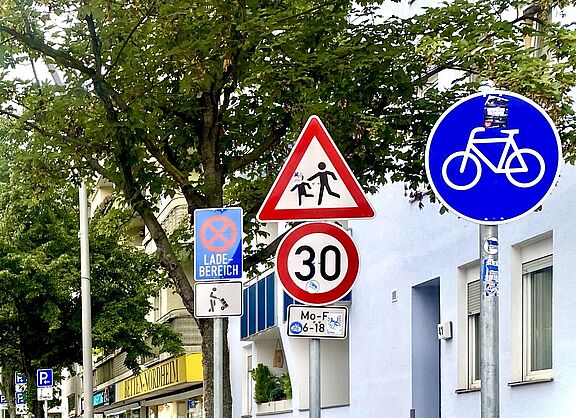 Auf dem Foto sind mehrere Verkehrszeichen zu sehen: Tempo 30, Kinder, benutzungspflichtiger Radweg, Lieferzone