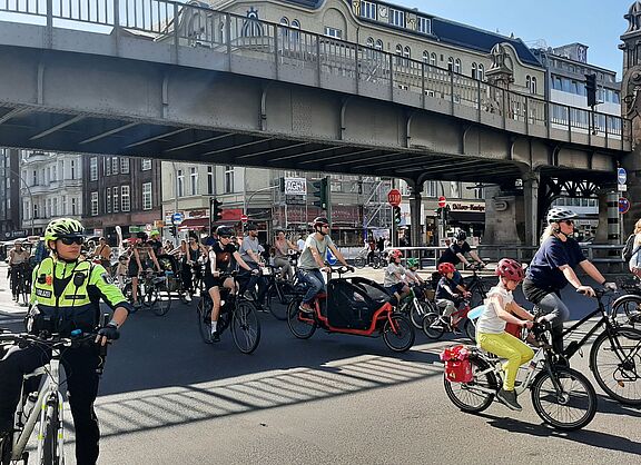 Eine Gruppe Erwachsener und Kinder fahren auf ihren Fahrrädern unter einer Brücke auf der Fahrbahn der Bülowstraße in Schönberg. Im Vordergrund ist eine Fahrradpolizistin zu sehen.