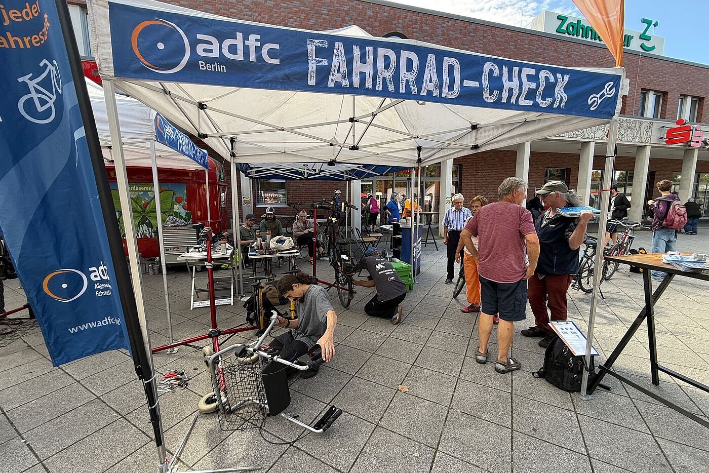ADFC-Fahrrad-Check 2025 Marzahn ADFC-Fahrrad-Check Pavillon mit Menschen die sich unterhalten und ein Mechaniker, der einen Rollator repariert