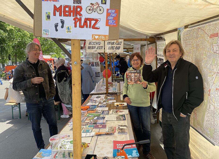ADFC Schöneberg und ADFC Tempelhof beim Nachbarschaftsfest 2025 Stand des ADFC Schöneberg und Tempelhof beim Nachbarschaftsfest am Schöneberger Rathaus am 24.05.2025 mit drei Standbetreuer:innen, die winken. Es sind Flyer, Fahnen und Plakate zu sehen.