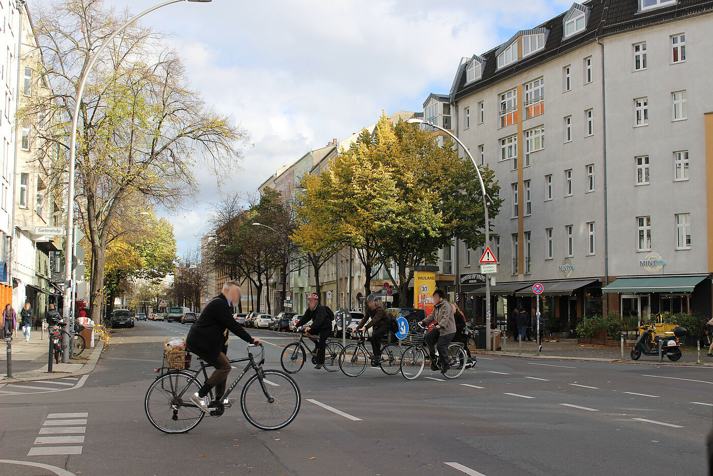 4 Radfahrer:innen fahren queren eine breite Innenstadtstraße