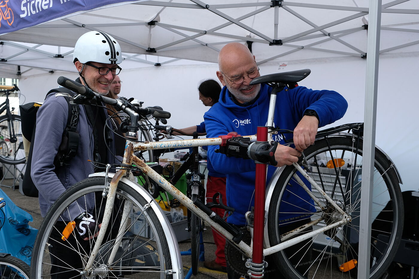 Fahrrad-Mechaniker repariert das Fahrrad eines Manns der mit Helm daneben steht