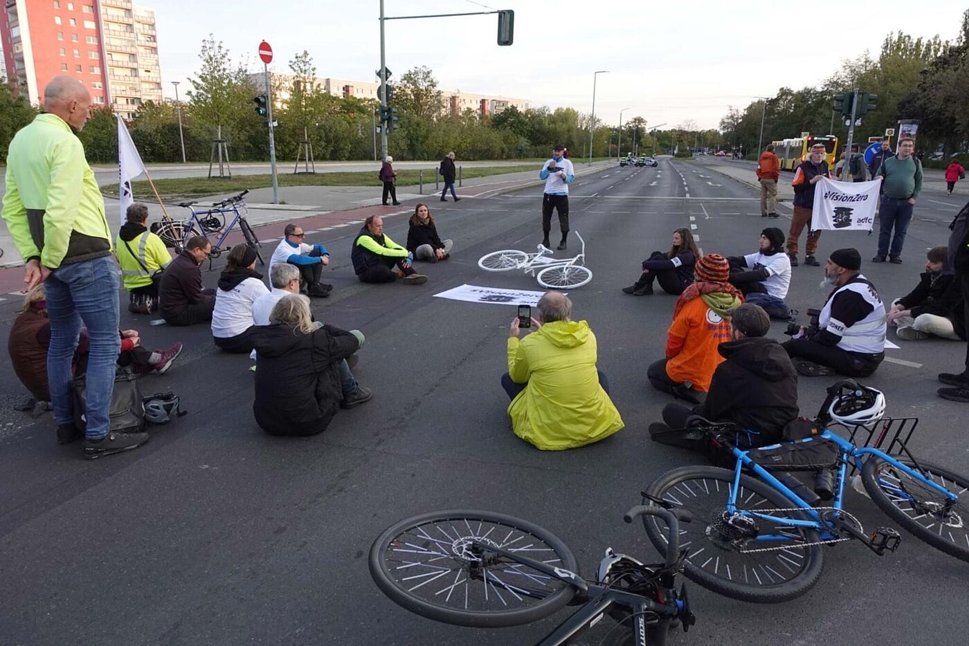 Menschen sitzen bei einer Mahnwache um ein weißes Geisterrad auf der Straße