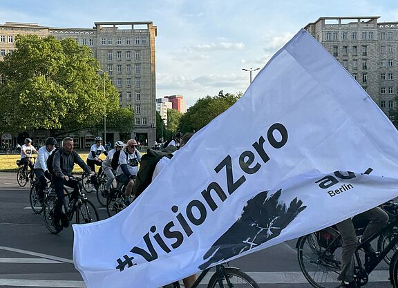 weiße Vision Zero Fahne weht vor Radfahrenden 