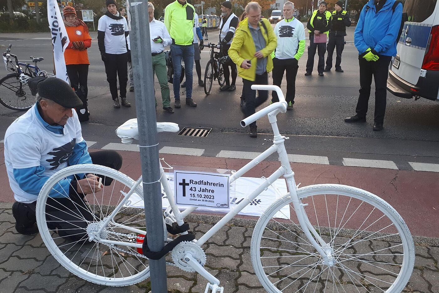 weißes Geisterrad für verstorbene Radfahrerin, Menschen gedenken im Hintergrund