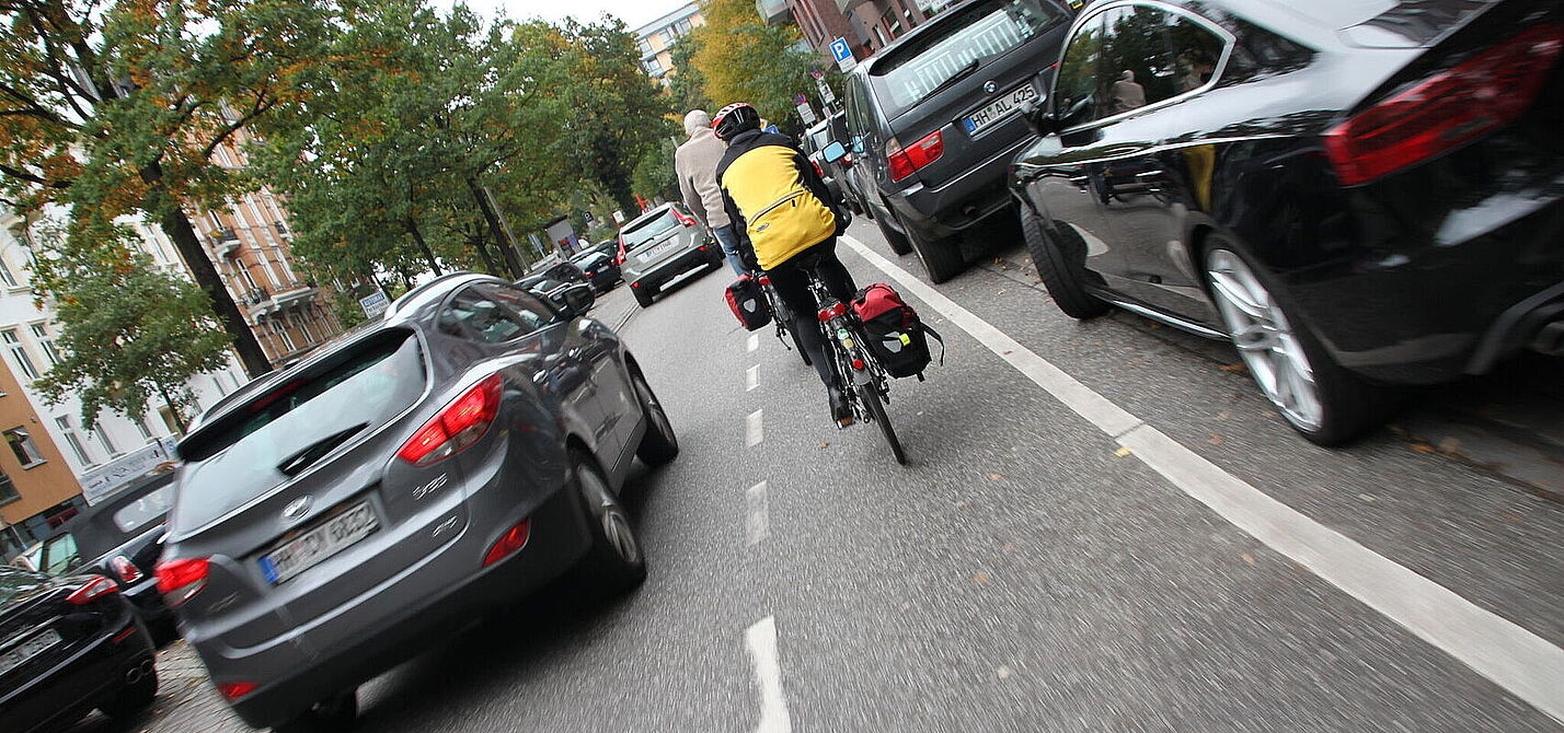 Radfahrender fährt neben parkenden Autos und wir von fahrenden Kfz zu knapp überholt.