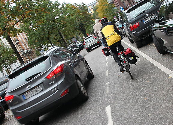 Radfahrender fährt neben parkenden Autos und wir von fahrenden Kfz zu knapp überholt.