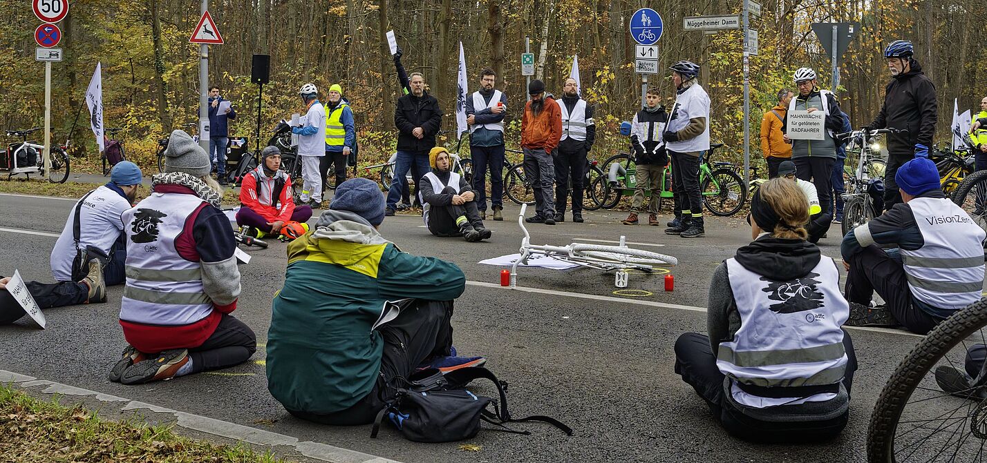 Menschen sitzen zur Mahnwache auf der Fahrbahn und gedenken eines getöteten Radfahrers