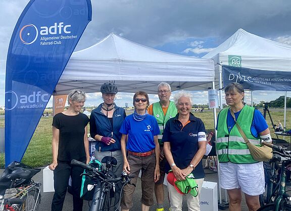 Aktive und Mitglieder verschiedener Stadtteilgruppen den ADFC Berlin stehen in einer Gruppe vor einem Stand des ADFC Berlin bei der Herzfahrt am 14.07.2024 auf dem Tempelhofer Feld