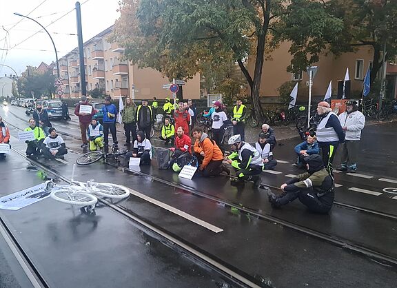 Menschen sitzen bei einer Mahnwache auf der Straße um ein weißes Geisterrad