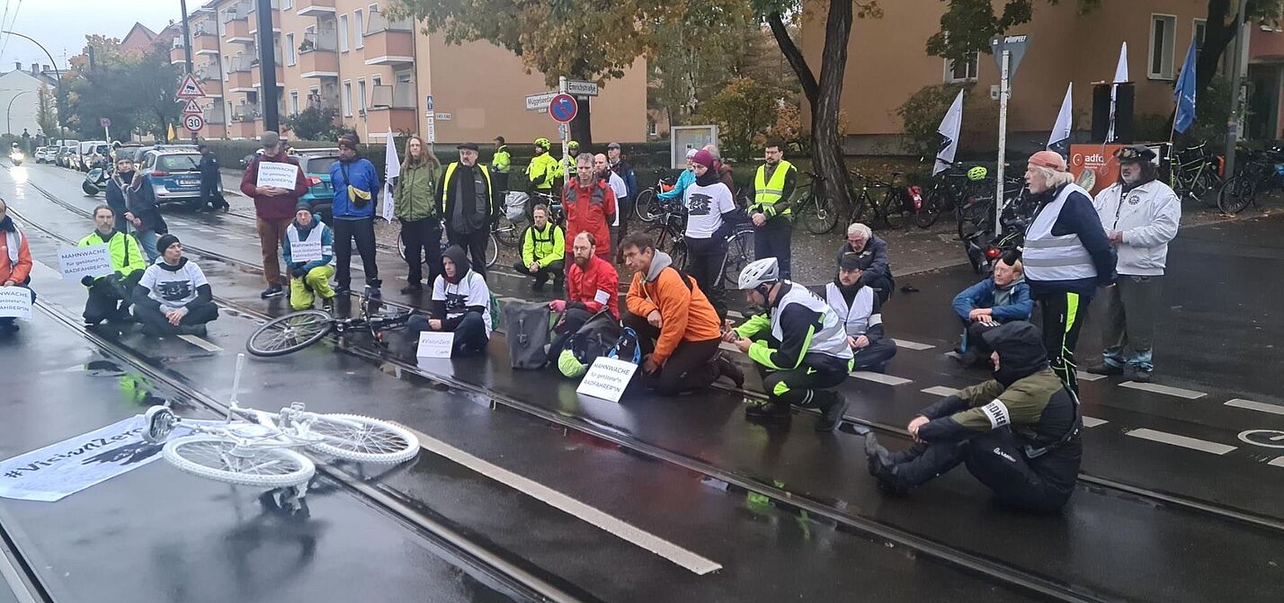 Menschen sitzen bei einer Mahnwache auf der Straße um ein weißes Geisterrad