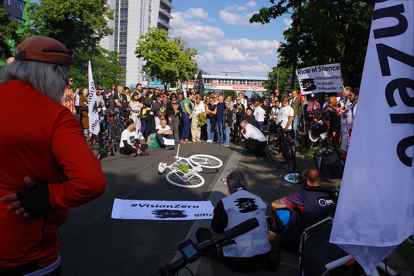 Menschen sitzen bei einer Mahnwache für einen getöteten Radfahrer auf der Straße um ein weißes Geisterrad