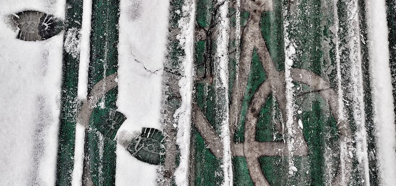 Man sieht eine grüne Bodenmarkierung eines Radwegs. Darüber liegt Schnee, der von Rad- und Fußabdrücken zerfurcht ist. 