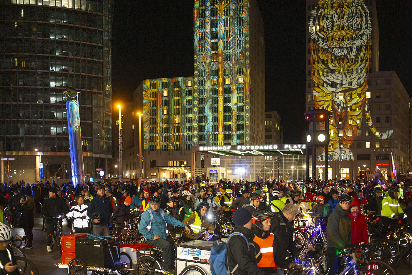 Menschen mit Fahrrädern auf dem Potsdamer Platz, Türme angestrahlt mit bunten Motiven