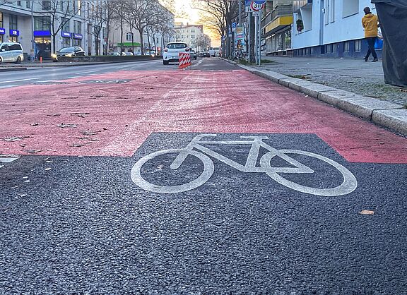 Auf der Fahrbahn der Grunewaldstraße ist ein geschützter Radweg mit Baken, roten Markierungen und einen Fahrradpiktogramm versehen.