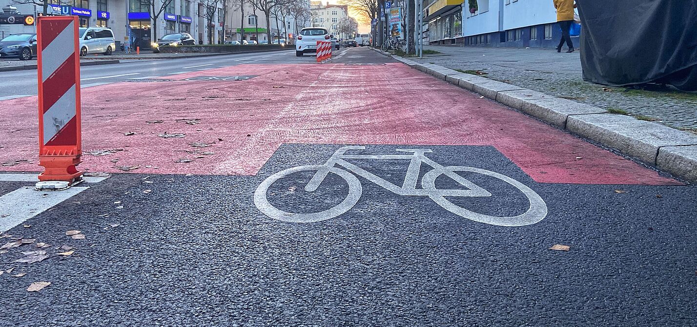 Auf der Fahrbahn der Grunewaldstraße ist ein geschützter Radweg mit Baken, roten Markierungen und einen Fahrradpiktogramm versehen.