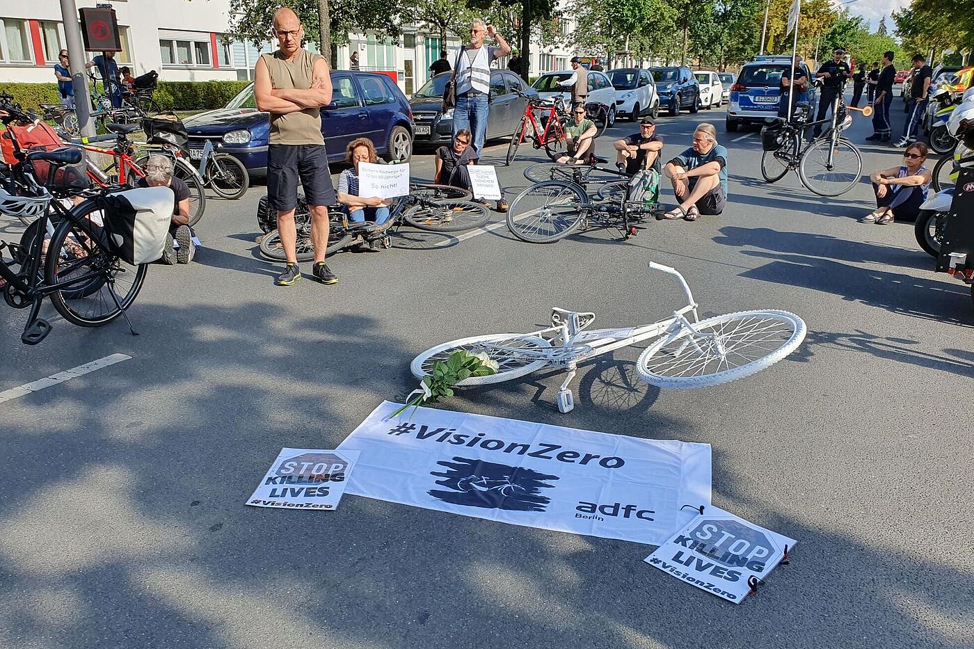 Menschen sitzen bei einer Mahnwache auf dem Boden um ein weißes Fahrrad