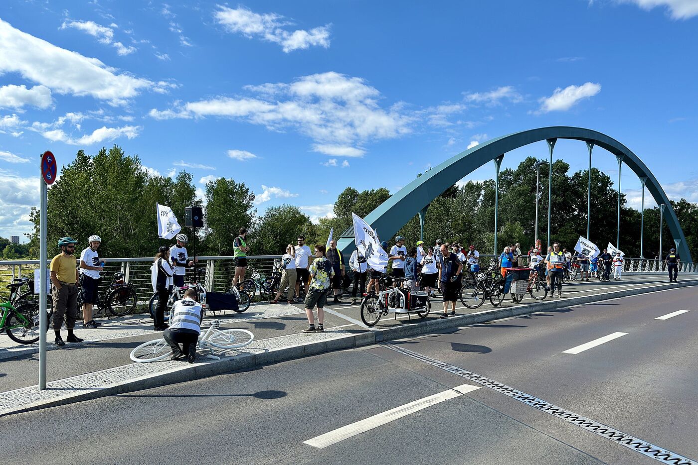 Menschen mit weißen T-Shirts stehen auf einer Brücke im Vordergrund ein weißes Geisterrad