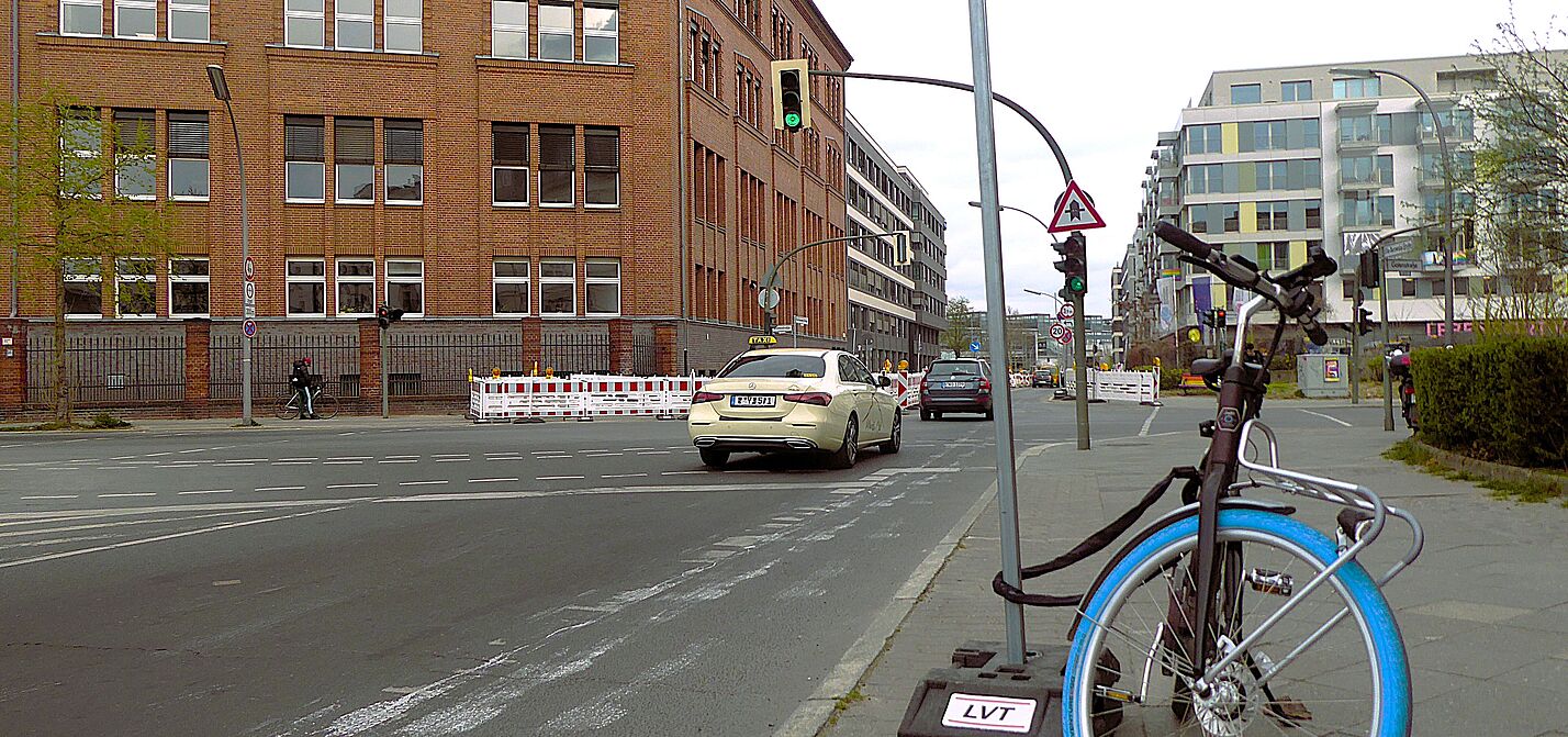 Die Ella-Barowsky-Straße und die Gotenstraße auf der Schöneberger Linse haben viel Kfz-Durchgangsverkehr Auf der Ella-Barowsky-Straße in Schöneberg fahren Richtung Bahnhof Südkreuz Autos. Es ist eine Kreuzung zu sehen, ein schmaler Radweg mit Piktogram, sowie ein Fahrrad, das am Ständer eines Baustellenschildes angeschlossen ist.