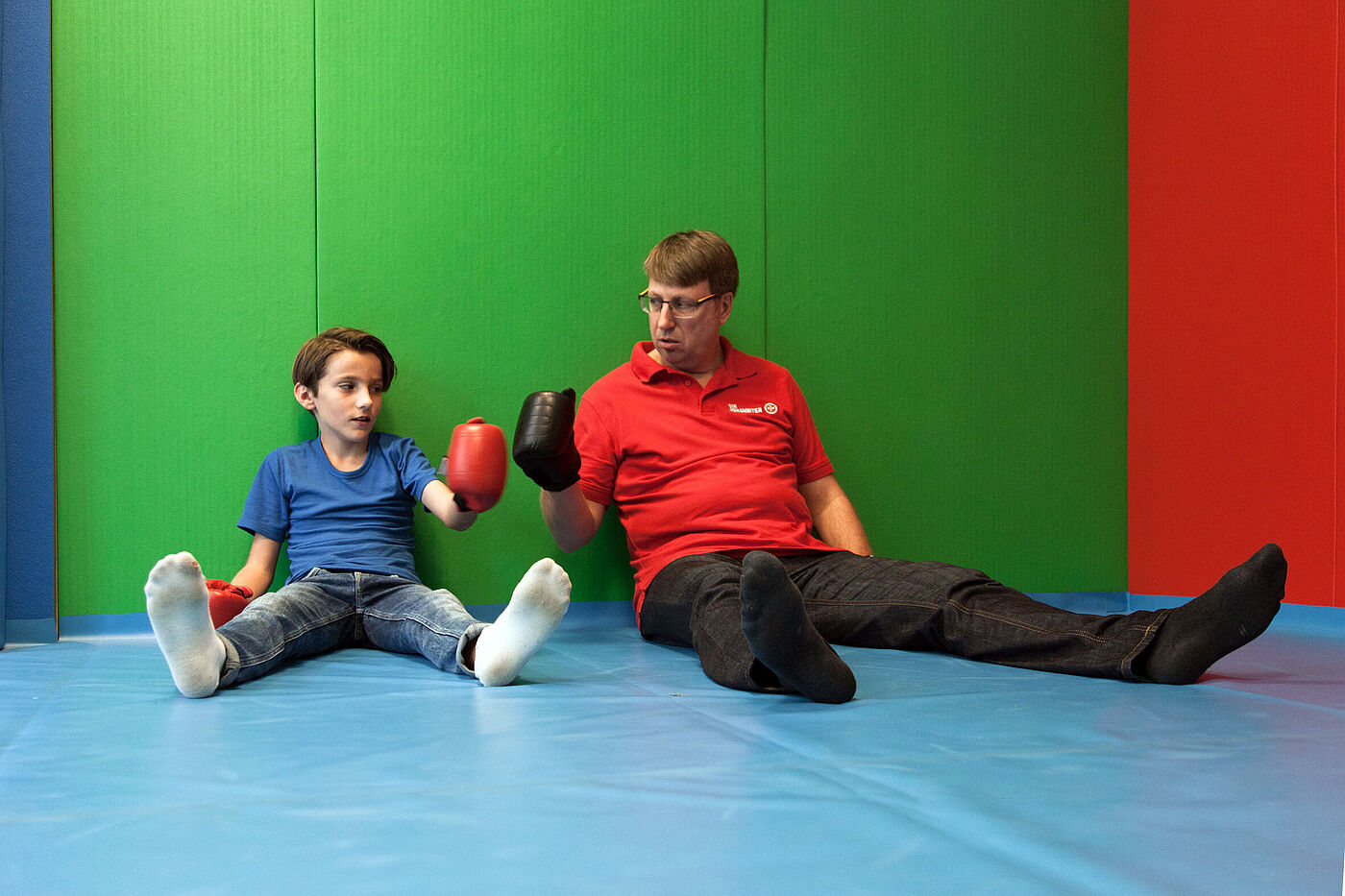 Ein Junge und ein Mann sitzen in einem Sportraum, der Junge trägt Boxhandschuhe