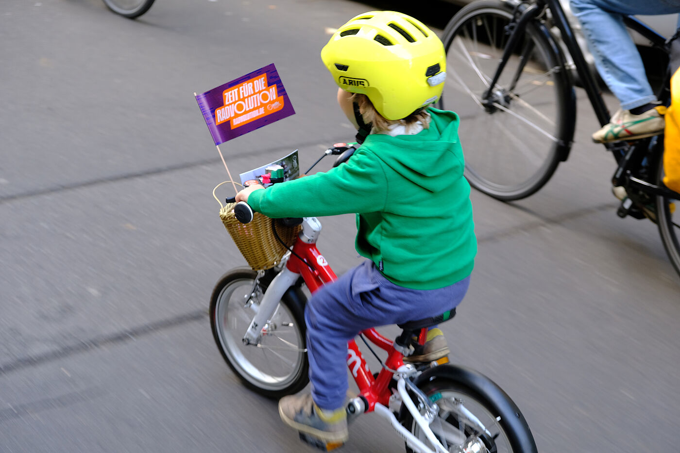 Kind mit gelbem Helm auf Fahrrad mit RADvolution Fähnchen