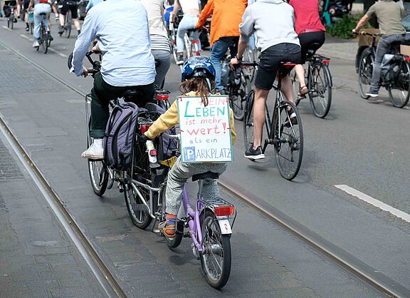 Mädchen auf Fahrrad mit einem Schild auf dem steht: Mein Leben ist mehr wert als ein Parkplatz