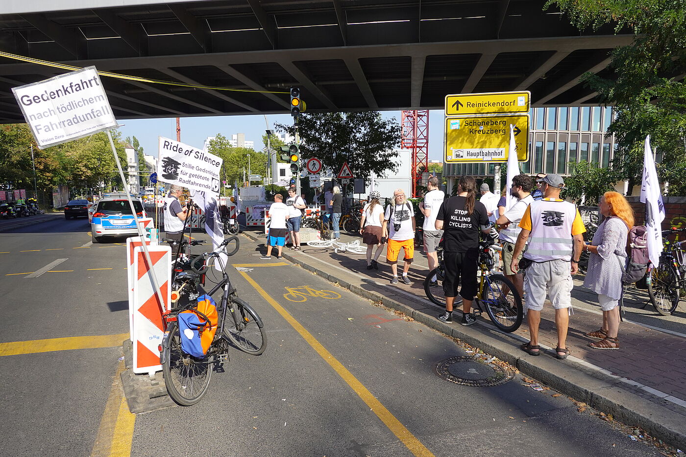 Demonstrierende mit weißen Vision Zero T-Shirts am Straßenrand neben Baustelle
