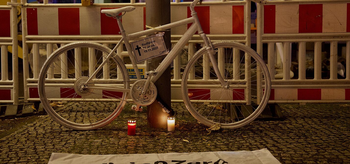 Geisterrad 24.11.2025 Mitte Ein weißes Geisterrad an einem Laternenphal davor eine weiße Vision Zero Fahne