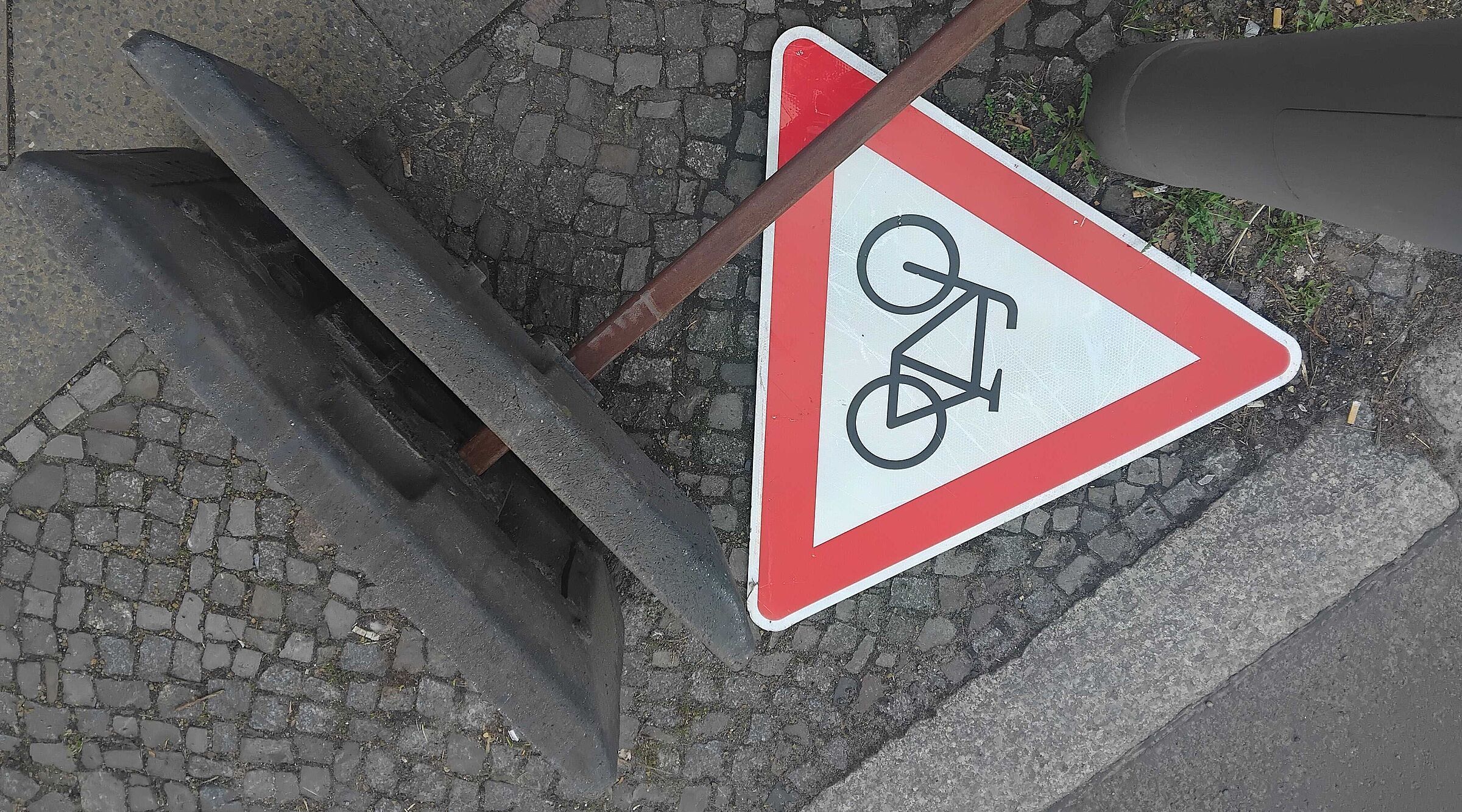 Das Bild zeigt ein rotes dreieckiges "Achtung Radfahrer"-Schild, es liegt auf dem Boden neben dem Fuß eines Baustellen-Aufstellers
