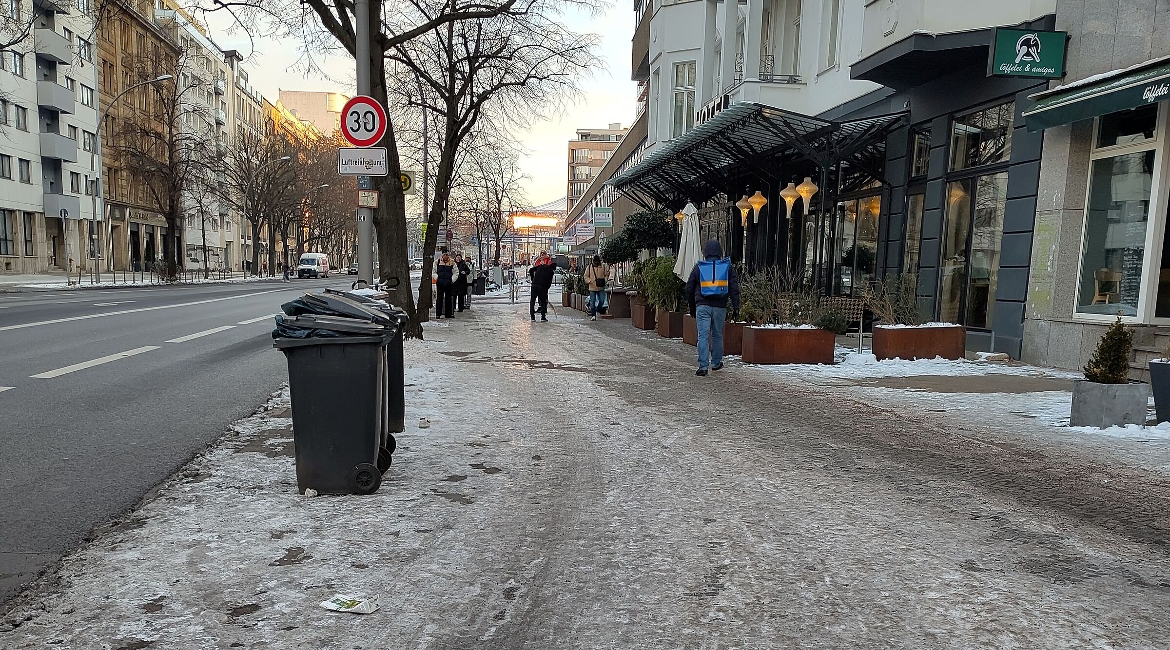 Im rechten Bereich ist ein vereister Gehweg und nicht erkennbar Radweg zu sehen, links davon ist Schnee- und Eis-freier Asphalt auf der Fahrbahn