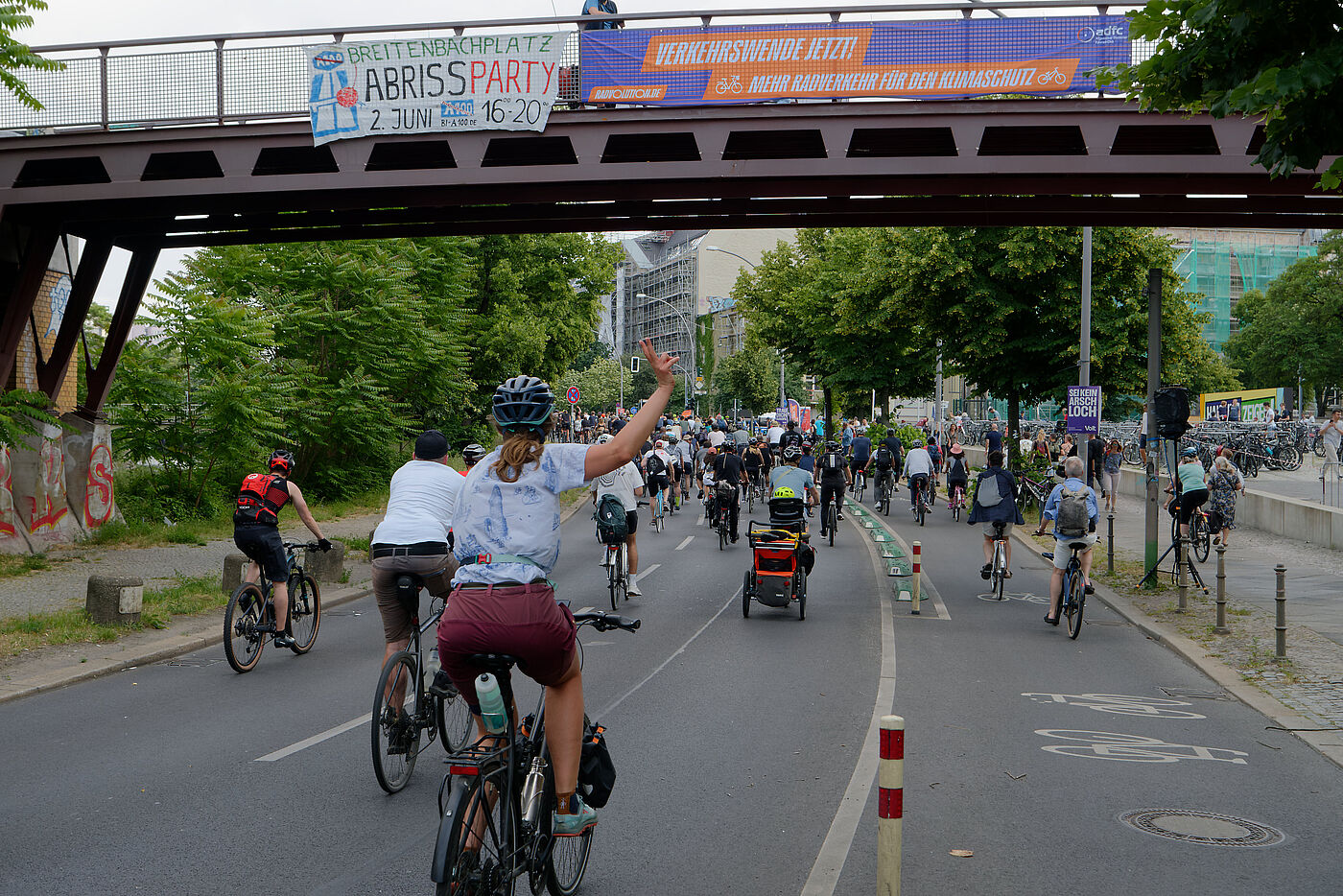 Menschen fahren auf dem Rad unter einer Brücke durch, behängt mit Transparenten