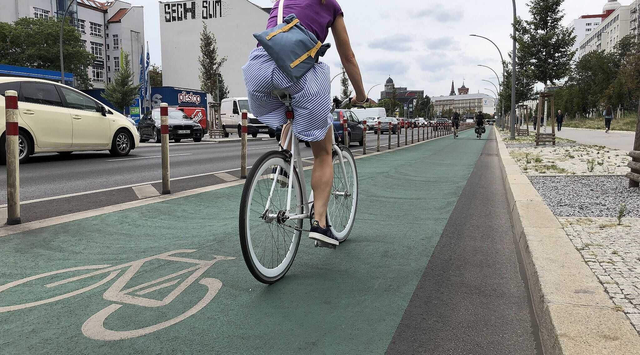 Eine Frau fährt auf einem grün markierten Radfahrstreifen mit Pollern vom Autoverkehr getrennt. 
