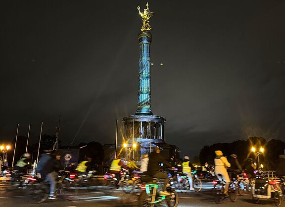 Siegessäule in Berlin wird angestrahlt, leuchtende Radfahrende herum