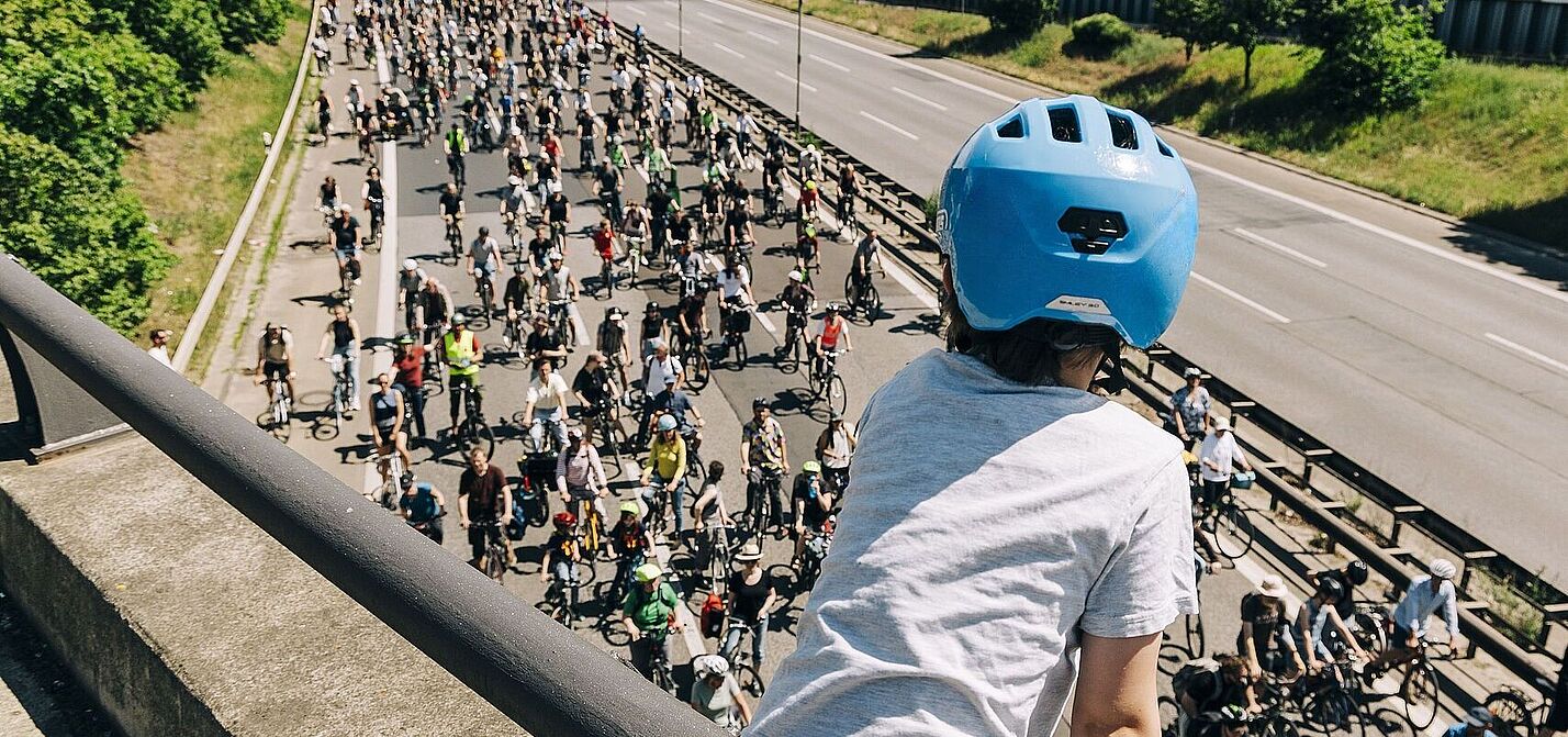 ADFC-Sternfahrt Kind mit blauem Helm guckt auf Autobahn über die auf einer Seite hunderte FahrradfahrerInnen fahren