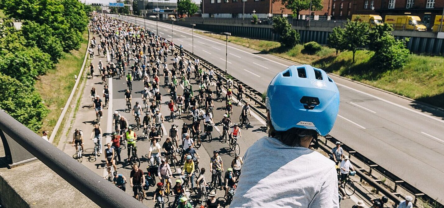 ADFC-Sternfahrt Kind mit blauem Helm guckt auf Autobahn über die auf einer Seite hunderte FahrradfahrerInnen fahren