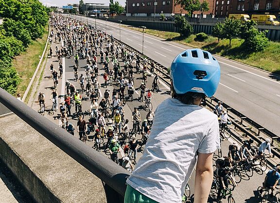 ADFC-Sternfahrt Kind mit blauem Helm guckt auf Autobahn über die auf einer Seite hunderte FahrradfahrerInnen fahren