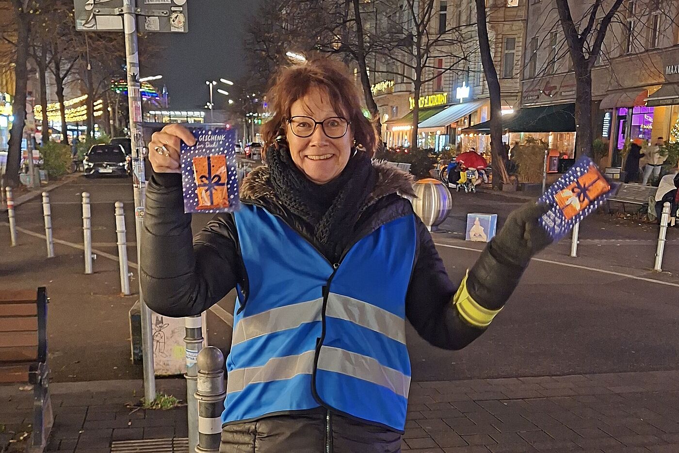 Eine Frau mit blauer Warnweste steht auf dem Winterfeldtmarkt in Berlin Schöneberg. Sie hält zwei Karten des ADFC mit einem Lebkuchen in Händen.